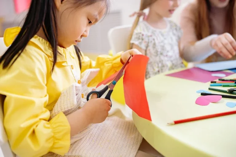 Niña recortando papel de colores con tijera