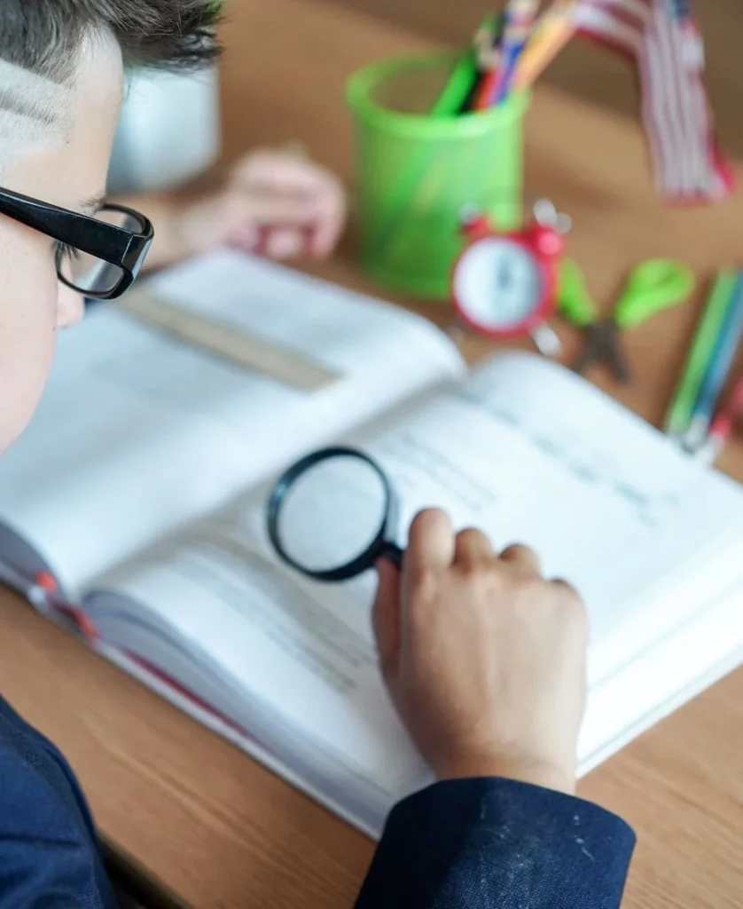 Niño observando un libro con una lupa