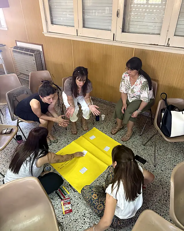 Docentes trabajan en equipo sobre un afiche en el piso